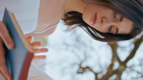 Romantic girl holding book sitting in beautiful nature vertical closeup. Attractive tranquil woman enjoy reading on summer calm morning. Relaxed young brunette relax alone on rye field landscape. - Footage, Video