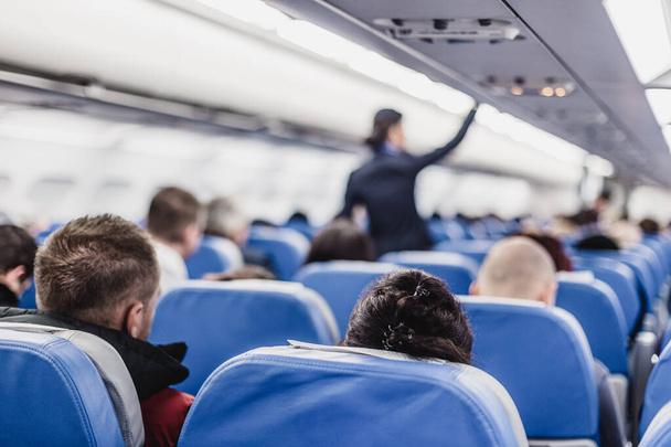 Interior del avión con pasajeros en asientos y azafata caminando por el pasillo. - Foto, imagen