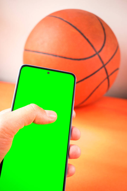 Smartphone mit grünem Bildschirm neben orangefarbenem Basketballball - Foto, Bild
