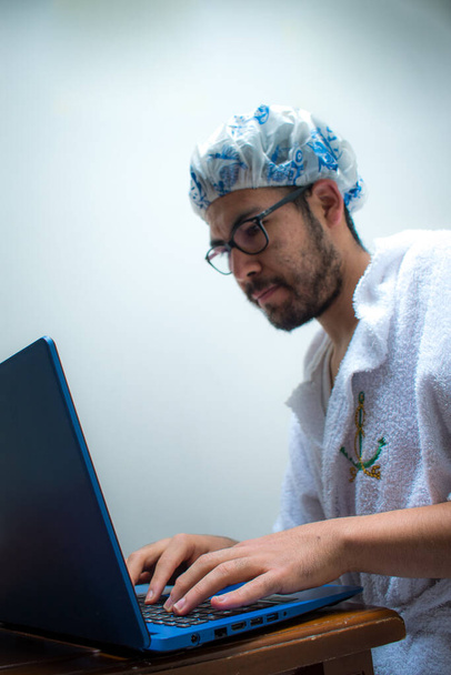 Homme portant serviette et bonnet de bain regardant ordinateur portable bleu  - Photo, image
