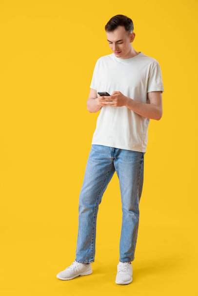 Young man with mobile phone messaging on yellow background - Photo, Image
