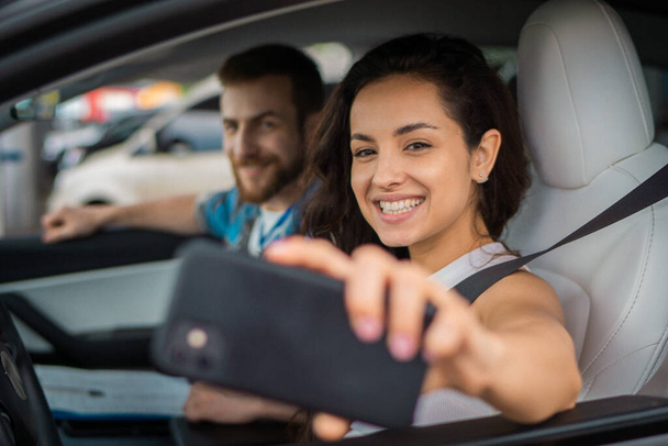 Usmívající se muž a žena sedí v autě během cesty, zatímco dělá selfie na mobilním telefonu. Cesta dobrodružné jízdy, šťastný letní dovolená koncept - Fotografie, Obrázek