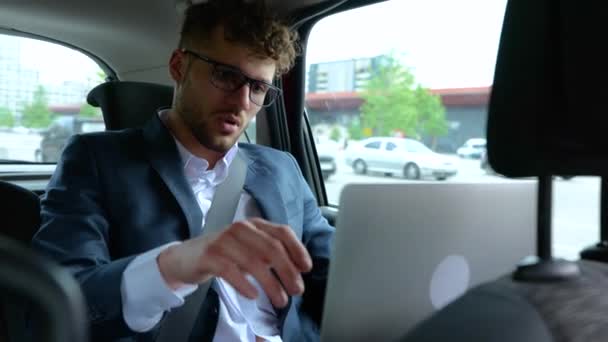 Młody biznesmen zamykający laptopa po ciężkiej pracy siedząc na tylnym siedzeniu taksówki. Biznes, podróże, transport i koncepcja technologii. Zwolniony ruch - Materiał filmowy, wideo