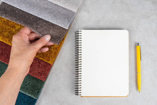 Renkli tekstil örnekleri, beyaz masa üzerinde not defteri ve kalem. El kumaş örneklerine dokunur, seçim için farklı renklerde ayarlanır. Mobilya ve iç döşeme malzemelerinin çeşitliliği. - Fotoğraf, Görsel