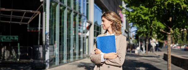 Portrait of businesswoman in beige suit and high heels walking on street. Corporate woman going to work, holding folder with documents. - Photo, Image