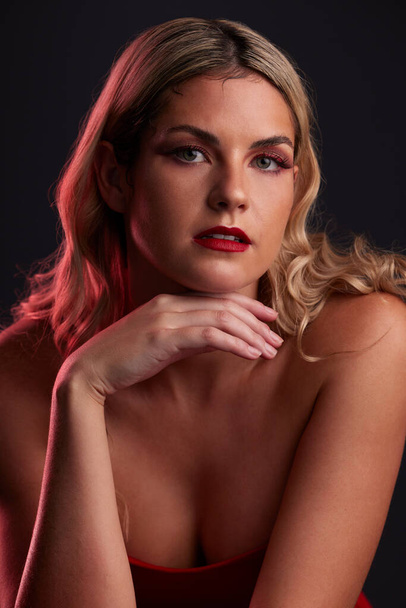 Portret, gezicht en schoonheid met een vrouw in de studio op een donkere achtergrond in rood licht voor verlangen. Huid, make-up of cosmetica met een jong vrouwelijk model poserend voor natuurlijk vrouwelijk vertrouwen. - Foto, afbeelding