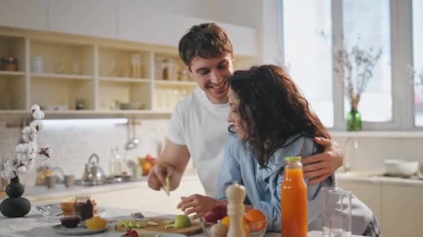 Romanttinen ystäville syö aamiaista viihtyisä keittiö nojaten työtaso lähikuva. Onnellinen, hymyilevä aviomies ruokkimassa kaunista naista omenaviipaleella. Iloinen rento pari nauttia perheen viikonloppuna kotona. - Materiaali, video