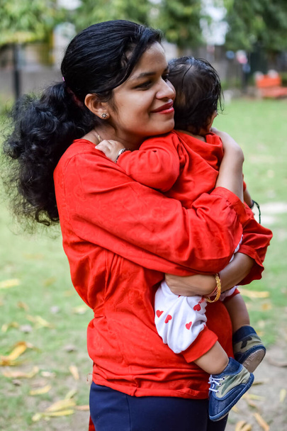 Loving mom carrying of her baby at society park. Bright portrait of happy mum holding child in her hands. Mother hugging her little 9 months old son. - Photo, Image
