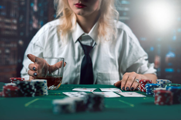 привлекательная девушка в рубашке и шляпе пьет виски и смотрит на покер карты в казино. Девушка-игрок делает ставку. покер в казино - Фото, изображение