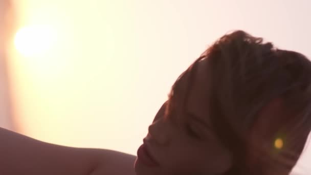 Függőleges portré egy fiatal nő fényes smink egy piros ruhát hátterében naplemente a tenger felett a sivatag közepén. Lassú mozgás, közelkép - Felvétel, videó
