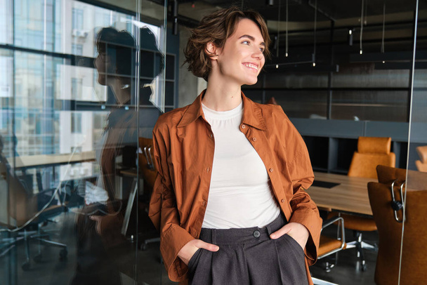Портрет красивой улыбающейся женщины на рабочем месте, работающей в офисе, имеет свой бизнес, глядя в сторону со счастливым, уверенным выражением лица. - Фото, изображение