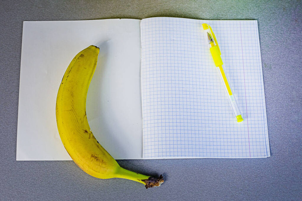 plátano en la mesa junto a un cuaderno de la escuela con bolígrafos amarillos. aperitivo escolar - Foto, imagen