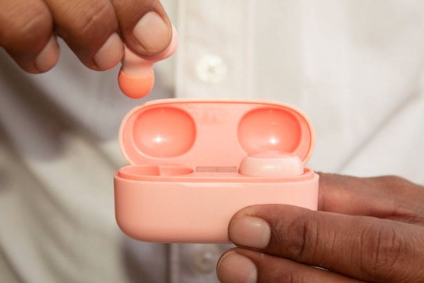 Close-up de uma mão masculina segurando um botões sem fio em um caso rosa - Foto, Imagem
