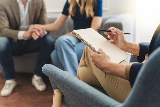 Couple therapy session: Therapist's notebook foregrounds while a young married couple holds hands in the background, seeking solutions to relationship challenges through counseling. - Photo, Image