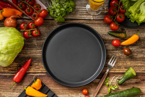 Assiette noire sur la table et la fourchette en bois, couteau avec poignée en bois, de nombreux légumes, vue sur le dessus - Photo, image
