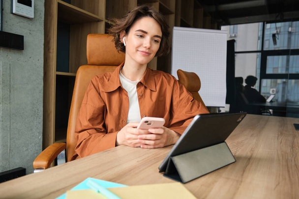 Portrait of female employee, start up entrepreneur in office, working with digital tablet, sitting in conference room waiting for team meeting. - Photo, Image