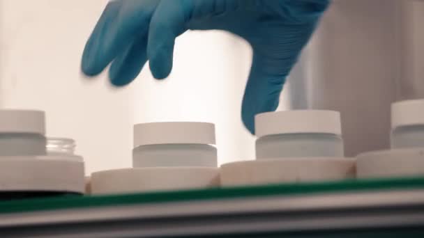 Ein Arbeiter verschließt kosmetische Cremeflaschen am Fließband - Filmmaterial, Video