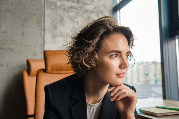 Foto profilo di donna d'affari sicura di sé pensando, meditando e guardando fuori dalla finestra, pensando a qualcosa al lavoro. - Foto, immagini