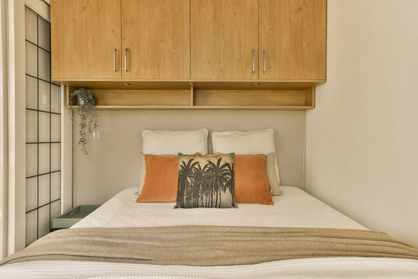 een bed in een kamer met houten kasten en kasten aan de muur erachter is een oranje kussentje - Foto, afbeelding