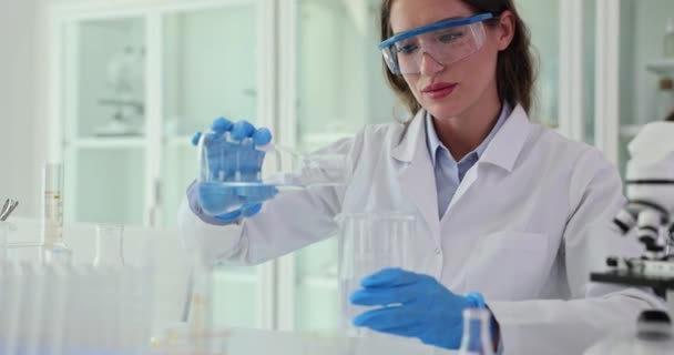 Tutkija kaataa vettä pullosta lasiin lääketieteellisessä laboratoriossa. Veden laadun testaus laboratoriossa - Materiaali, video