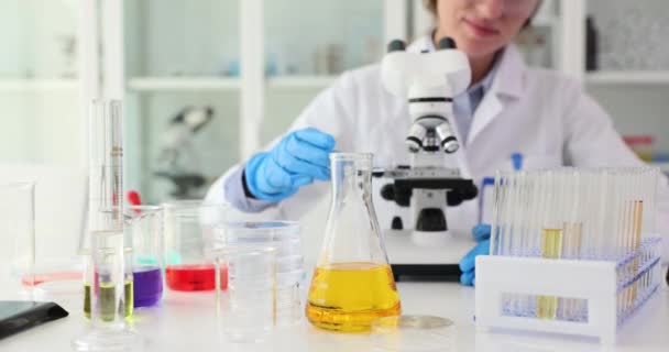 化学科学者は,化学実験室で黄色い液体または油を有する顕微鏡を介して見ています. 石油製品と石油の研究 - 映像、動画
