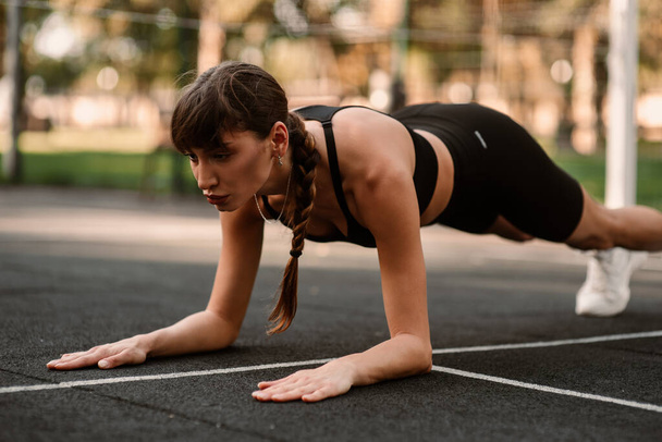 Een jonge vrouwelijke trainer voert een fitness compressie-oefening uit. Het meisje traint buiten. Een gezonde levensstijl. Hoge kwaliteit foto - Foto, afbeelding