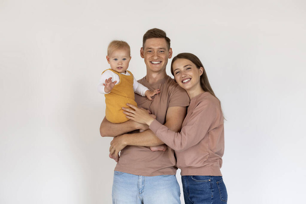 Glückliche junge Eltern, die ihren süßen Kleinkindsohn halten und in die Kamera lächeln, Porträt einer schönen fröhlichen dreiköpfigen Familie mit kleinem Baby, das gemeinsam vor weißem Hintergrund posiert, Kopierraum - Foto, Bild