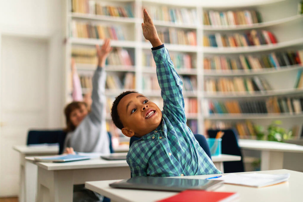 Разнообразные школьники, сидя за партами и с энтузиазмом поднимая руки во время урока в начальной школе, воплощают в себе стремление к обучению и активному участию в образовательной среде - Фото, изображение