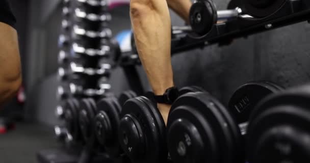 Man hand takes dumbbell out of set of black weights. Sports training and dumbbell weight selection - Footage, Video