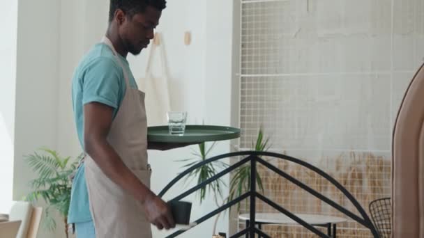 Μέτριο πλάνο Αφρο-Αμερικανού σερβιτόρου να παίρνει πιάτα και γυναίκα Καυκάσια υπάλληλος καφετέριας να σκουπίζει τραπέζια την ημέρα - Πλάνα, βίντεο