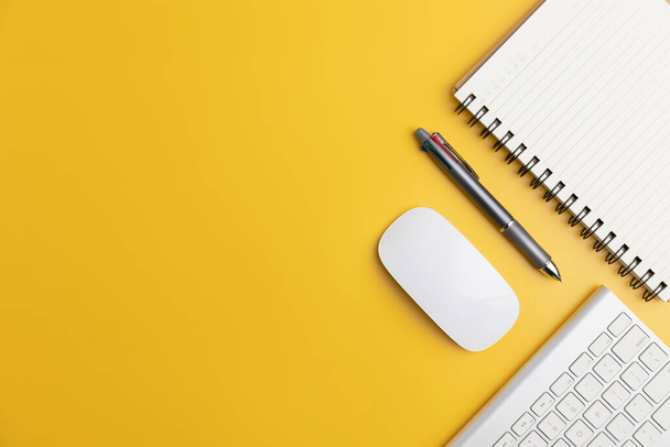 Het thuiskantoor met een pen, en notebook met een muis op een gele tafel met kopieerruimte. Bovenaanzicht, plat lag minimaal geel bureauconcept. Werkruimte bureau met toetsenbord op gele achtergrond. - Foto, afbeelding