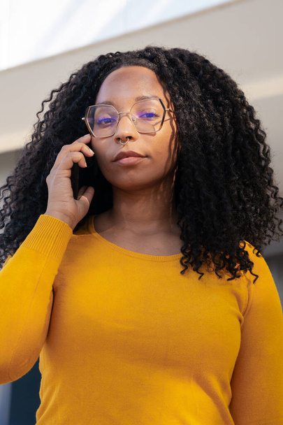 Mavi güneş gözlüğü takan güzel siyahi kadın cep telefonundan kızgın konuşuyor. - Fotoğraf, Görsel
