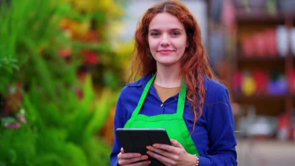 Портрет молодой женщины-менеджера, держащей планшет и носящей зеленый фартук в розничном магазине - Кадры, видео