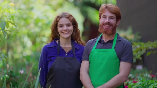 Portrait de deux jardiniers heureux dans des tabliers, entrepreneurs horticoles dans un environnement vert - Séquence, vidéo