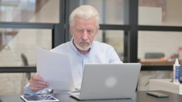 Vecchio uomo d'affari si sente sconvolto durante la lettura del contratto e utilizzando il computer portatile - Filmati, video