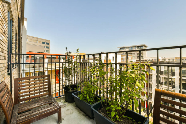 een balkon met een aantal planten in de potten en een bank aan de andere kant van het balkon, er is een blauwe lucht - Foto, afbeelding