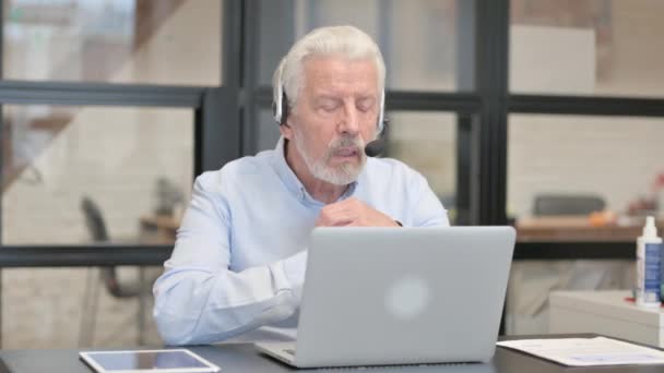 Hombre viejo con auriculares haciendo chat de vídeo en el ordenador portátil en el centro de llamadas - Metraje, vídeo