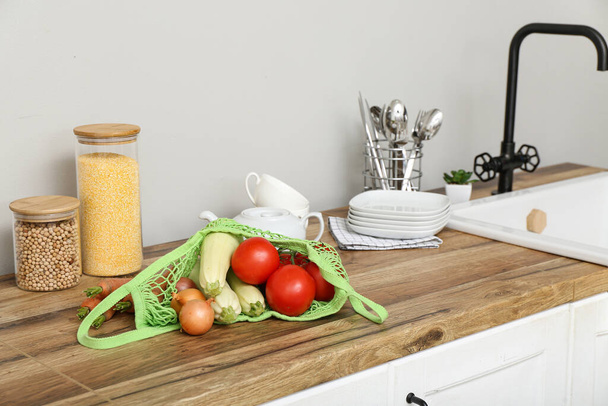 Bolsa de malla con diferentes verduras frescas en el mostrador en la cocina - Foto, imagen