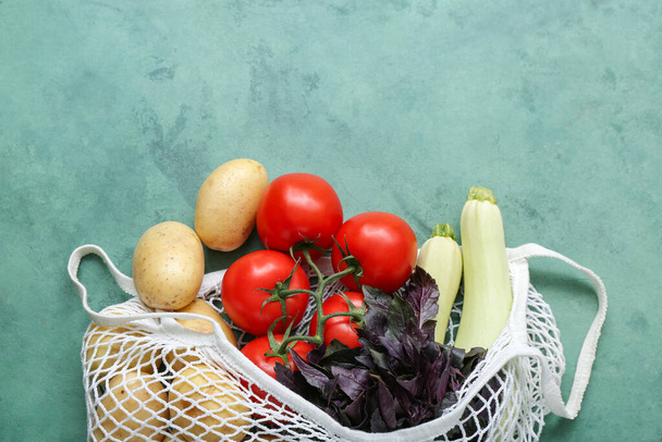 Mesh bag with different fresh vegetables on green background - Photo, Image