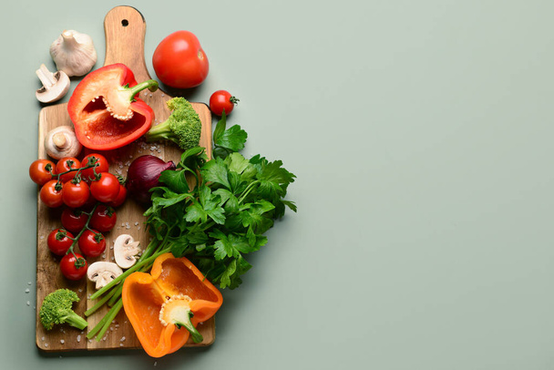 Wooden board with fresh vegetables and greenery on grey background - Photo, Image