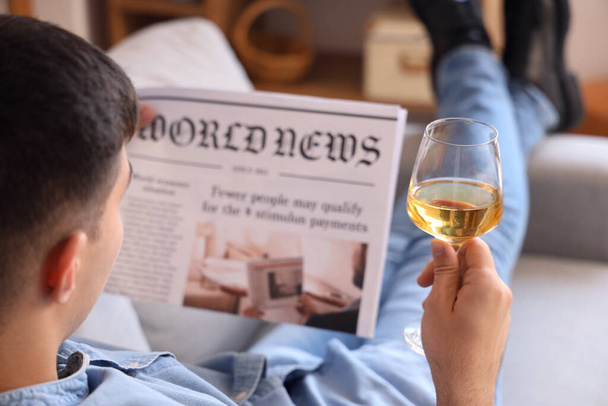 Νεαρός άνδρας με ποτήρι κρασί ανάγνωση εφημερίδα στο σπίτι, closeup - Φωτογραφία, εικόνα