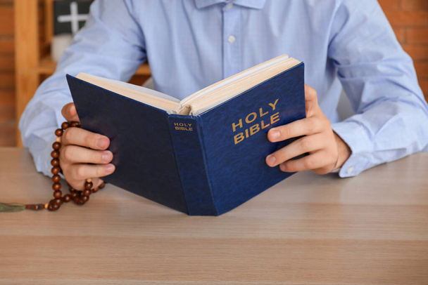 Mladý muž s růženec korálky čtení Bible u dřevěného stolu, detailní záběr - Fotografie, Obrázek