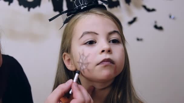 Mulher fazendo halloween make-up para uma menina alegre pouco no traje enquanto prepara férias em casa. Imagens FullHD de alta qualidade - Filmagem, Vídeo