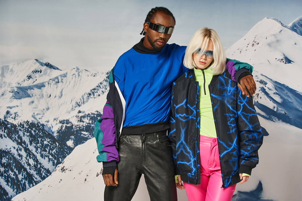 young interracial couple hugging and looking at camera with mountain backdrop, winter concept - Photo, Image