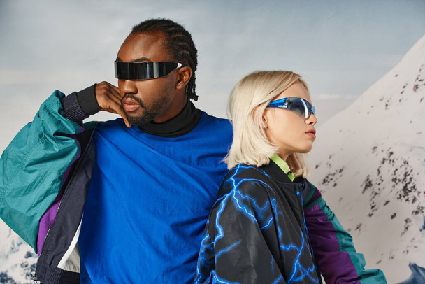 módní pár ve stylových slunečních brýlích pózujících spolu s horským pozadím, zimní koncept - Fotografie, Obrázek
