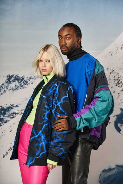 attractive young multicultural couple in stylish winter attire hugging and posing on snowy backdrop - Fotó, kép