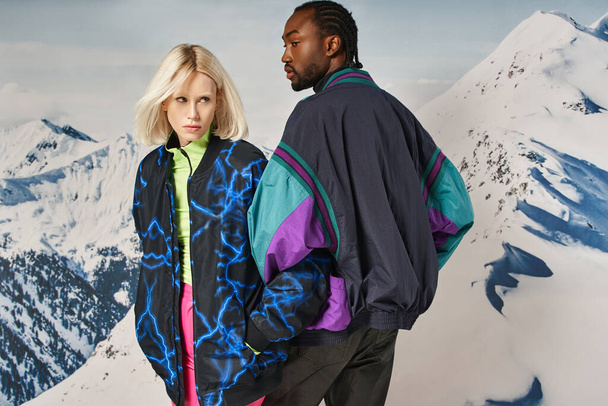 mladý stylový pár v teplém zimním oblečení pózovat spolu se zasněženým horským pozadím - Fotografie, Obrázek