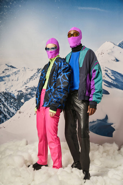 Pembe kar maskeli, güneş gözlüklü, kalın elbiseli, çok kültürlü bir çift, kış konsepti. - Fotoğraf, Görsel