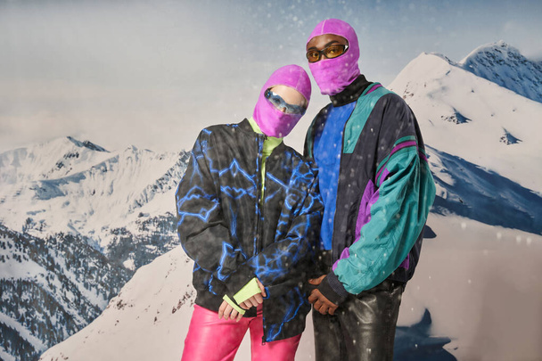 κομψό ζευγάρι σε ζωντανή φωτεινό ντύσιμο με γυαλιά ηλίου με φόντο το βουνό, έννοια του χειμώνα - Φωτογραφία, εικόνα