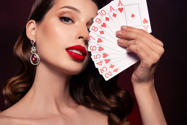 Foto der eleganten Dealerin, die im Pokerclub spielt, zeigt ihr gewinnendes Kartenvermögen vor dunklem Hintergrund. - Foto, Bild